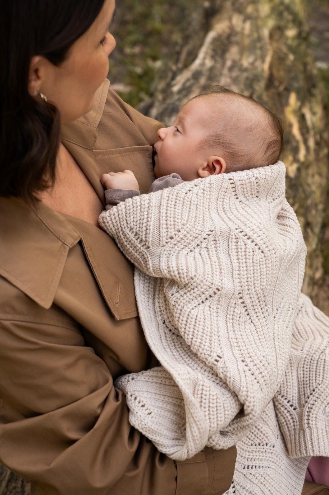 Mor holder baby svøbt i et beige merinould babytæppe – blødt, varmt og åndbart