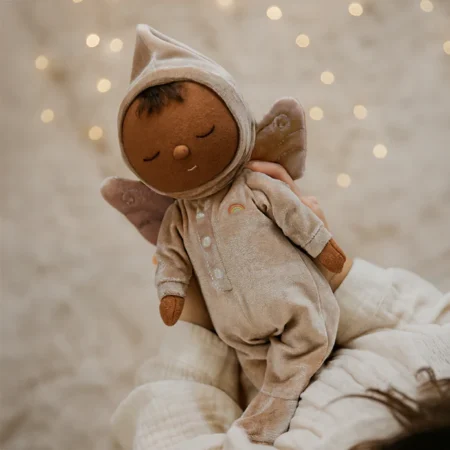Fairy Ada dukke fra Olli Ella – blød Dozy Dinkum dukke i beige velourdragt med fevinger, holdt i hænderne foran varm baggrund med lys.