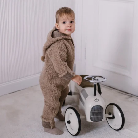 Barn iført brun ulddragt til baby står ved legebil – viser den bløde og varme kvalitet i Zaffiro Nevada ulddragt.