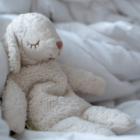 Senger Naturwelt varmebamse formet som et lille får i økologiske materialer, liggende i seng og skaber tryg og beroligende varme til baby og barn